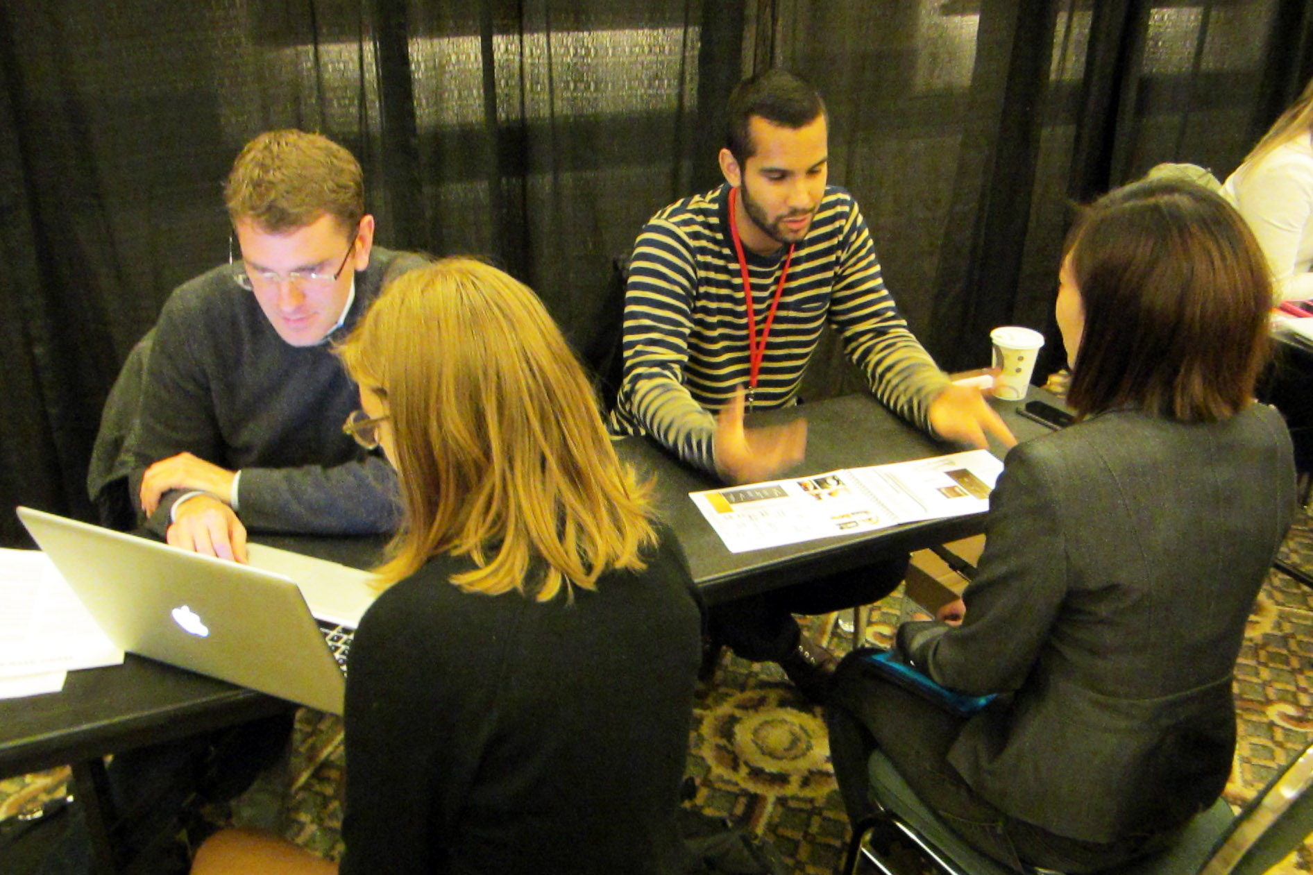 A photo of four people seated at a table looking at a computer and papers