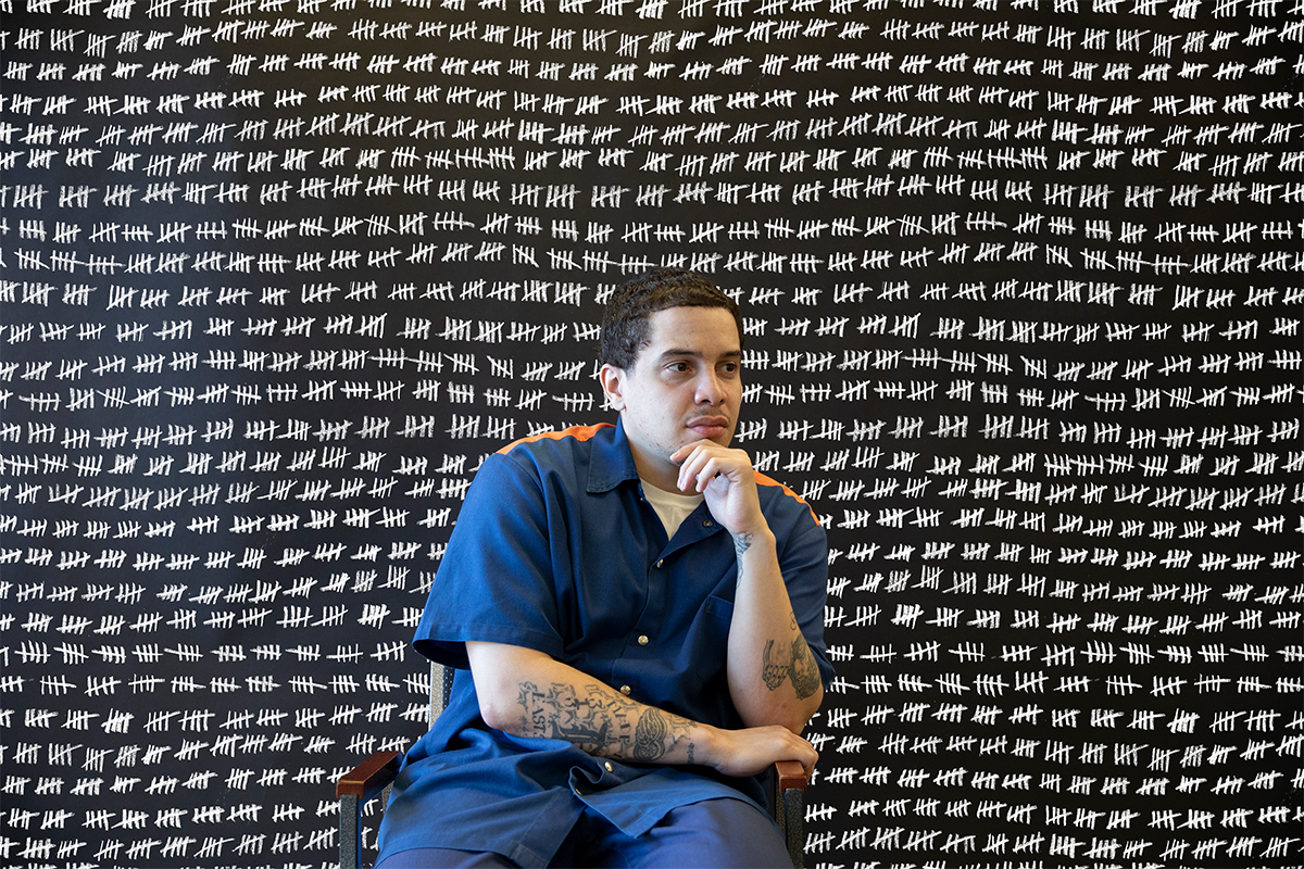A man sitting in front of a black background filled with white tally marks
