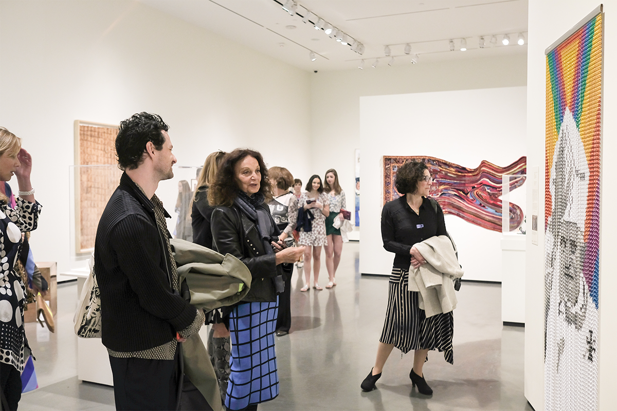 Image of people in a gallery space looking at prints and textiles on the wall 