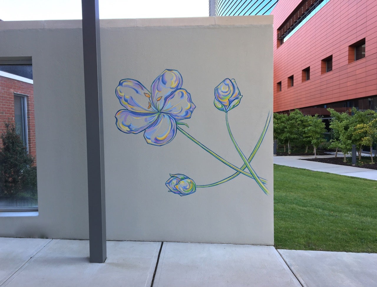 A photograph of the mural Flower Walk showing a multicolored flower in the foreground and a green lawn and building in the background.
