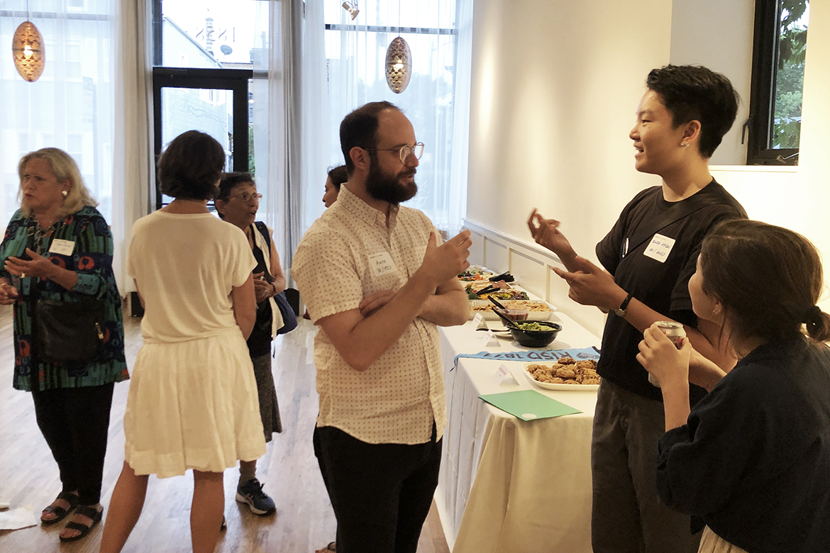 Aumni chat in groups at a Volunteer Info Session while enjoying food and drink in a light and airy event space.