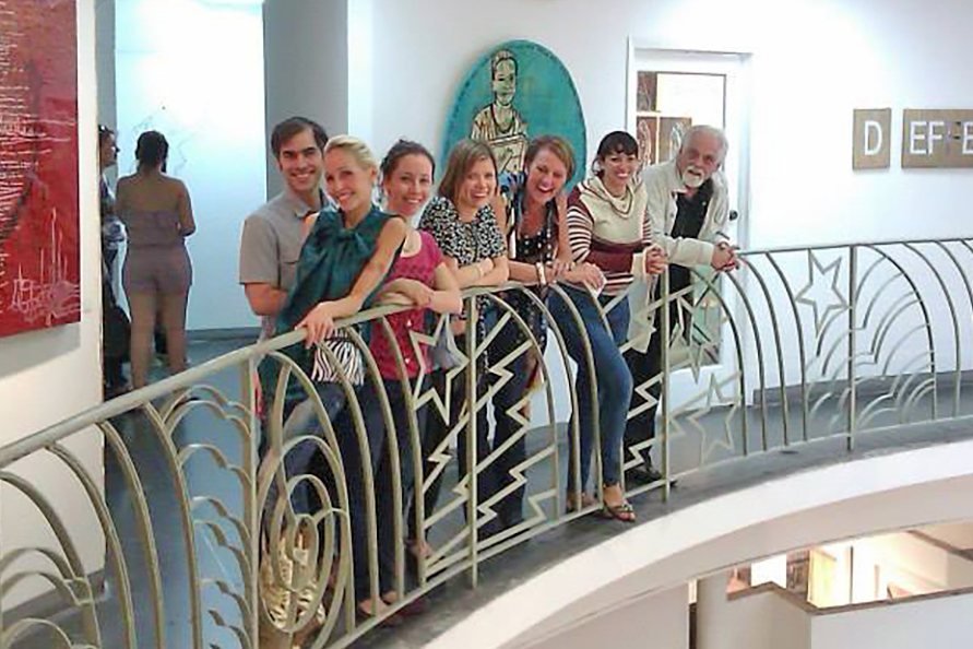Photo of a group of people posing at a railing in a multi-level gallery for a Miami Club event.