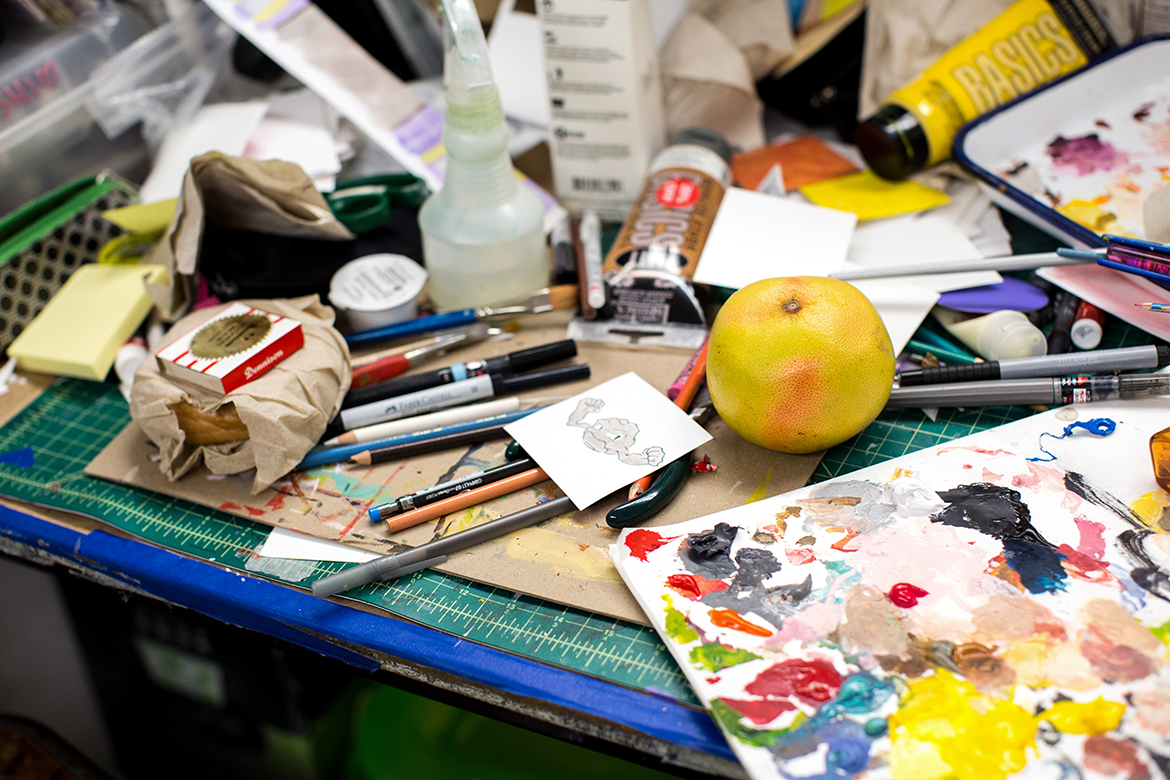 Photo of studio desk top detail with sharpies, paint, rulers, a grapefruit, etc.