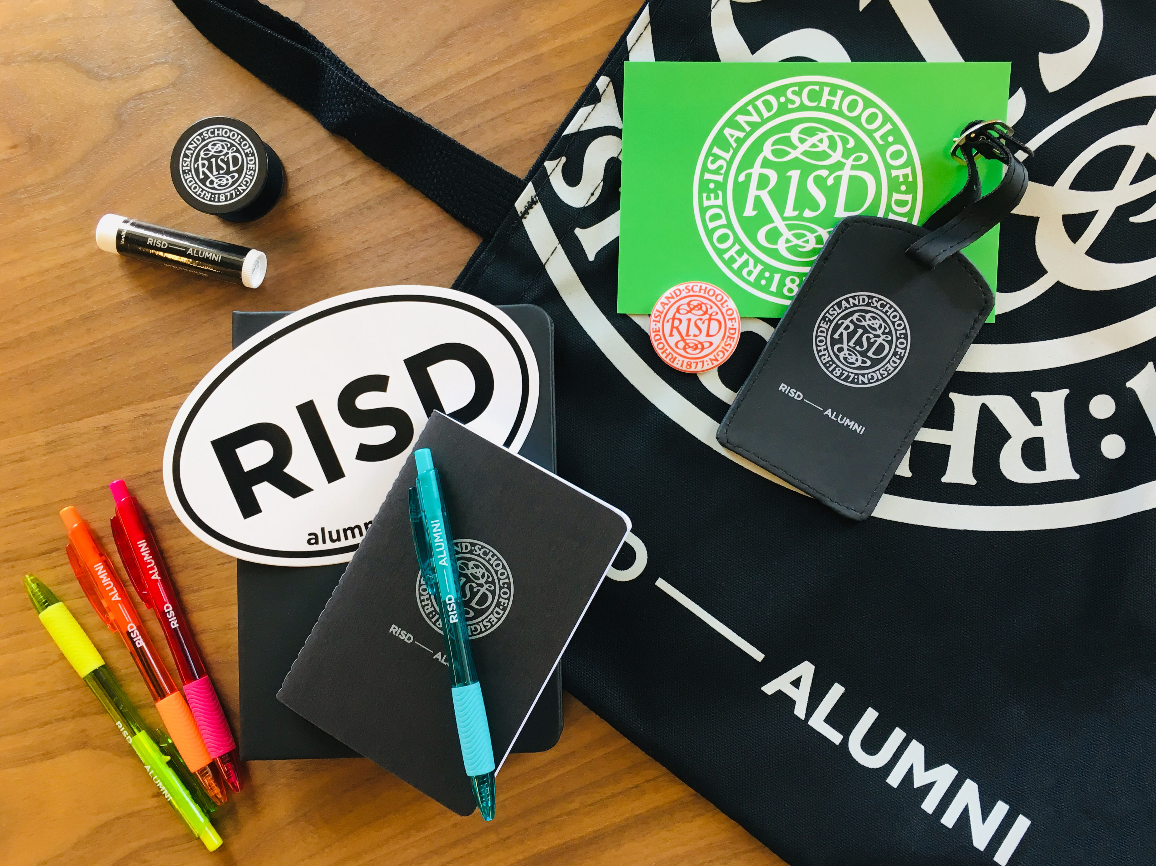 Photo of RISD swag on a table: pens, buttons, totebag, luggage tag, etc.