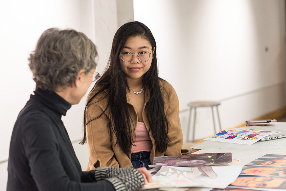 Student speaking with another person with drawings in front of them.