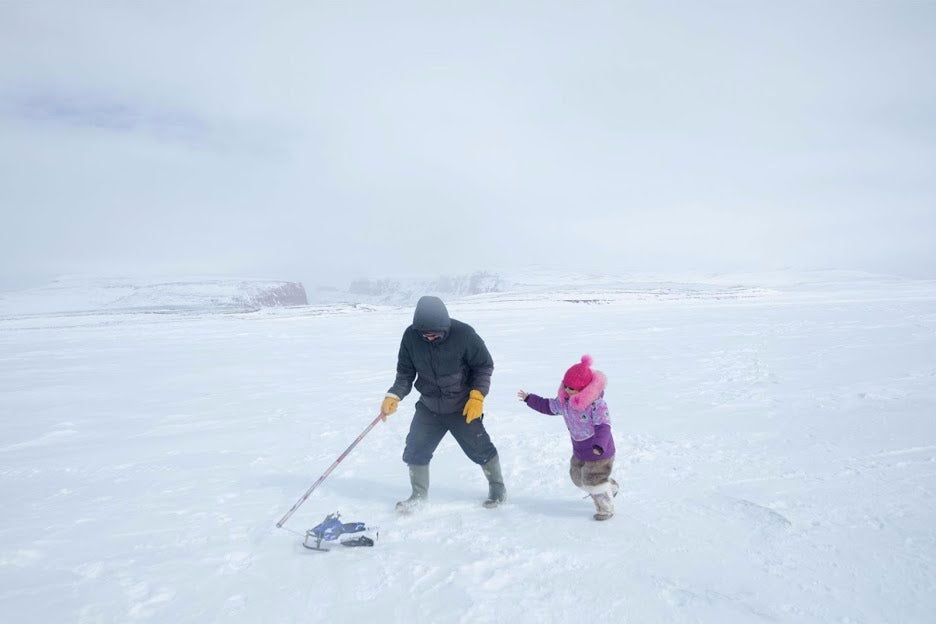 Man pulls a toy snowmobile for his daughter.