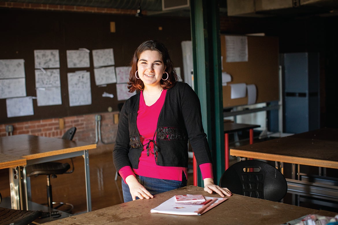 Photo of Shelby Bernard standing in the studio with some of her graphic design work