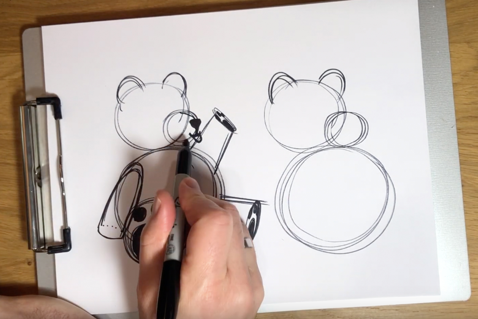 A hand drawing a sketch of a teddy bear.
