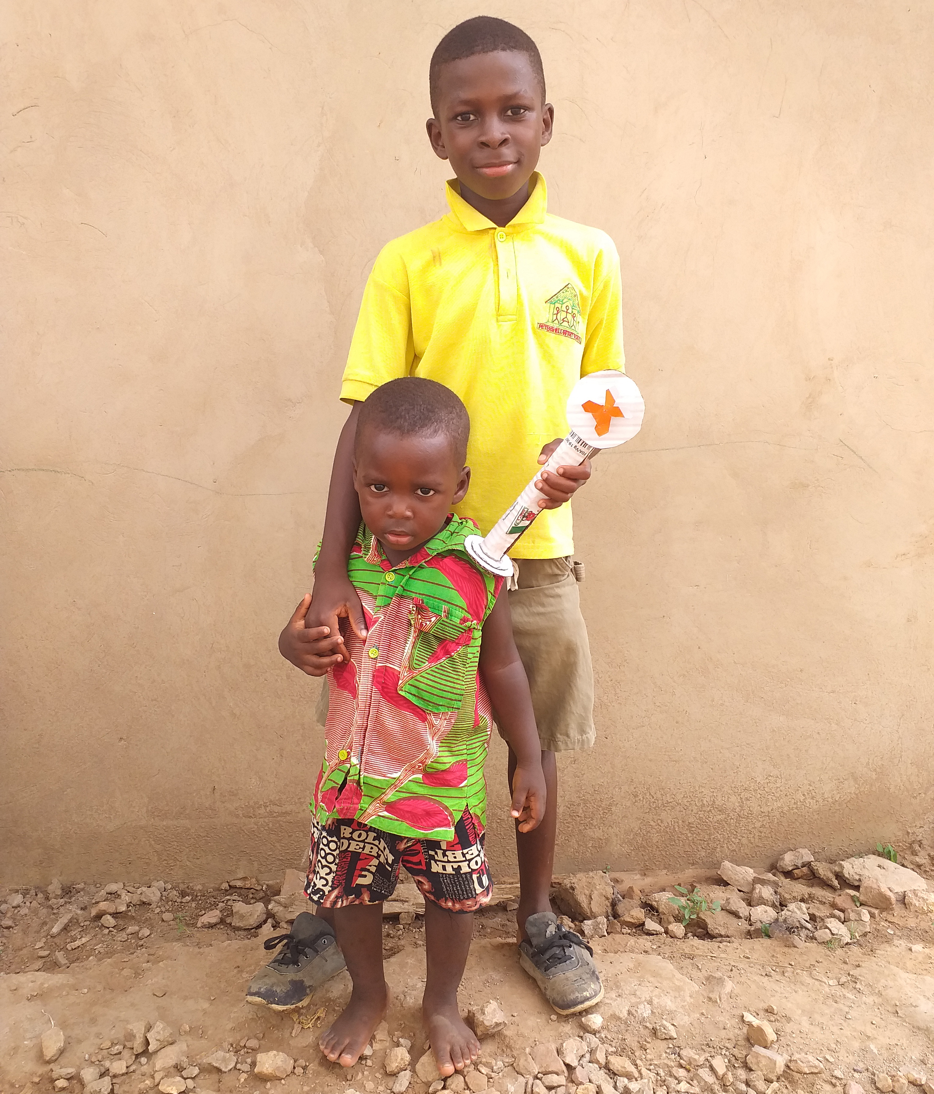 Posed photo of two children, standing against a tan wall. 