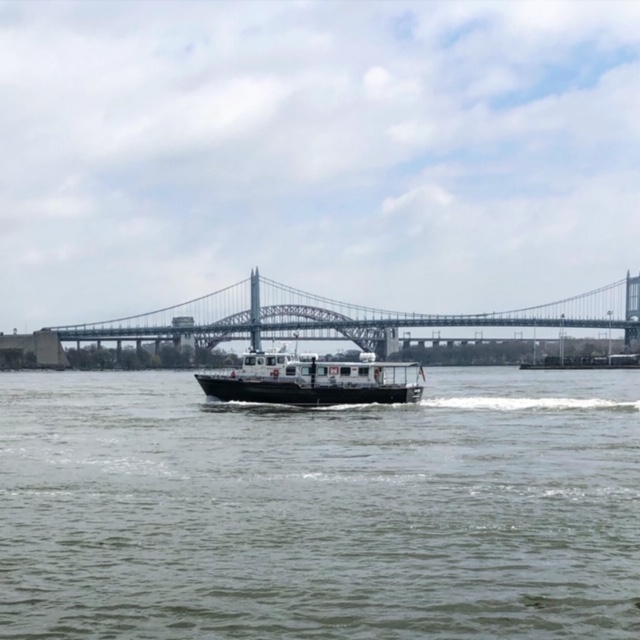 A view of a boat on a river in NYC, with two bridges in the background.