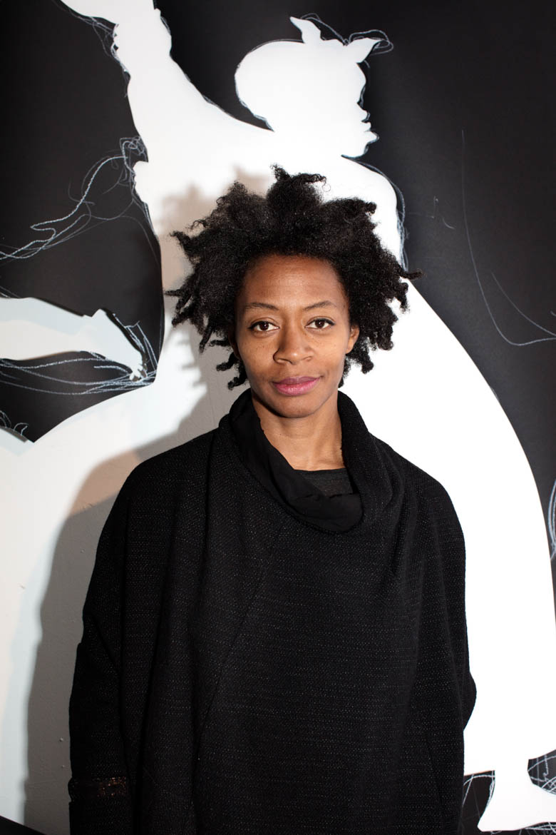 Kara Walker standing in front of a silhouette drawing.