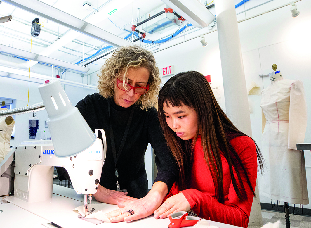 An image of RISD President Rosanne Somerson working with a student at a sewing machine