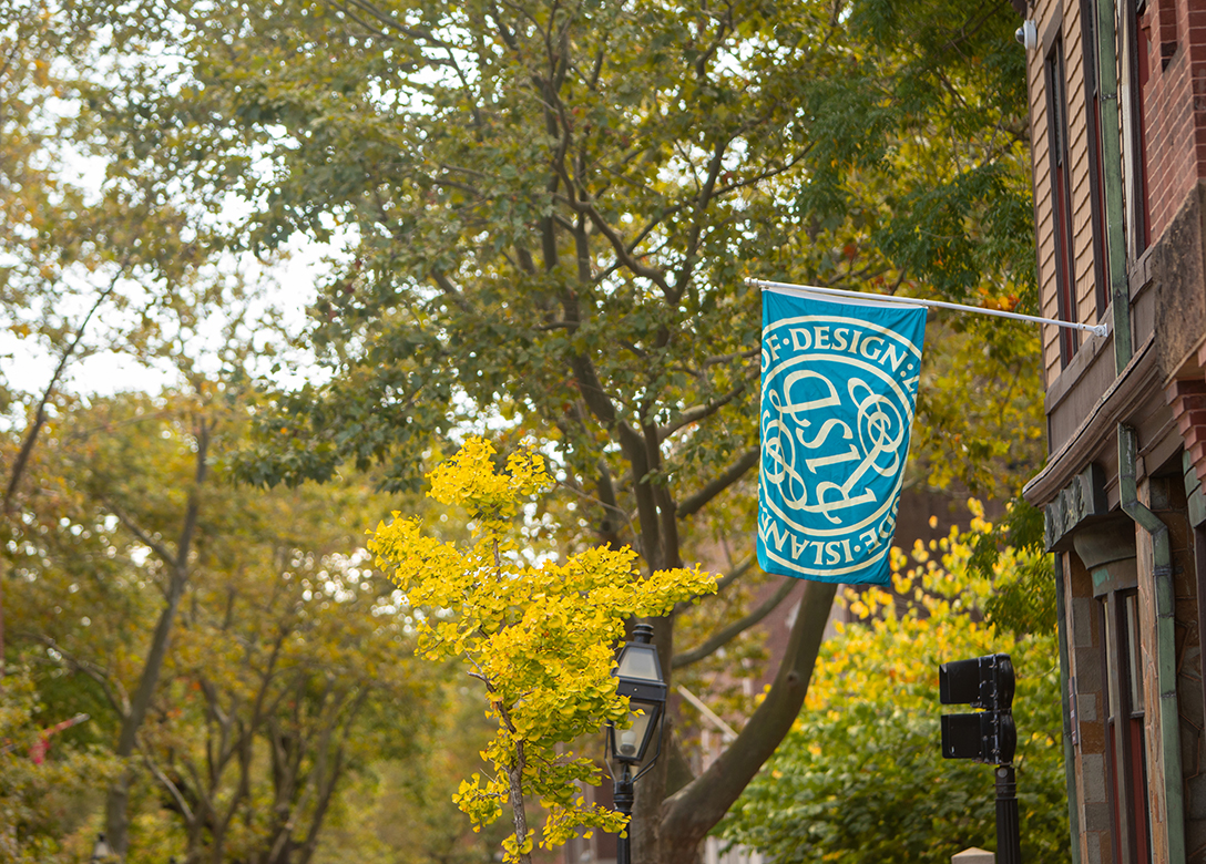 An image of RISD campus featuring trees and a turquoise banner with the RISD insignia