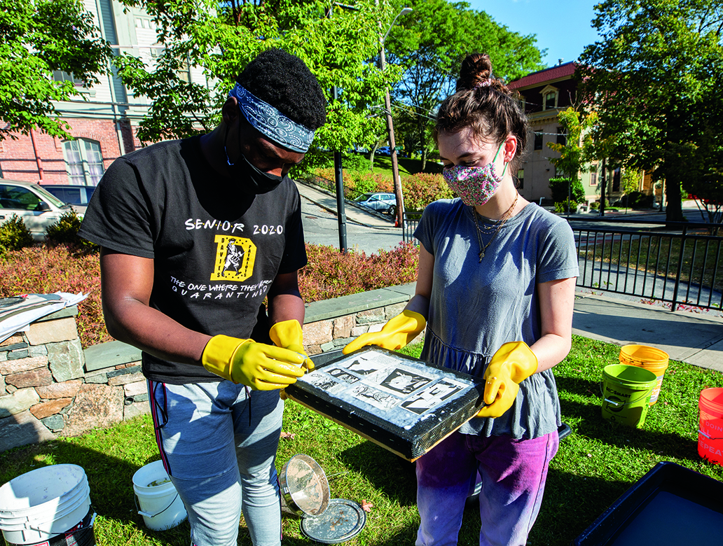Image of two students working outdoors on a project wearing masks. 