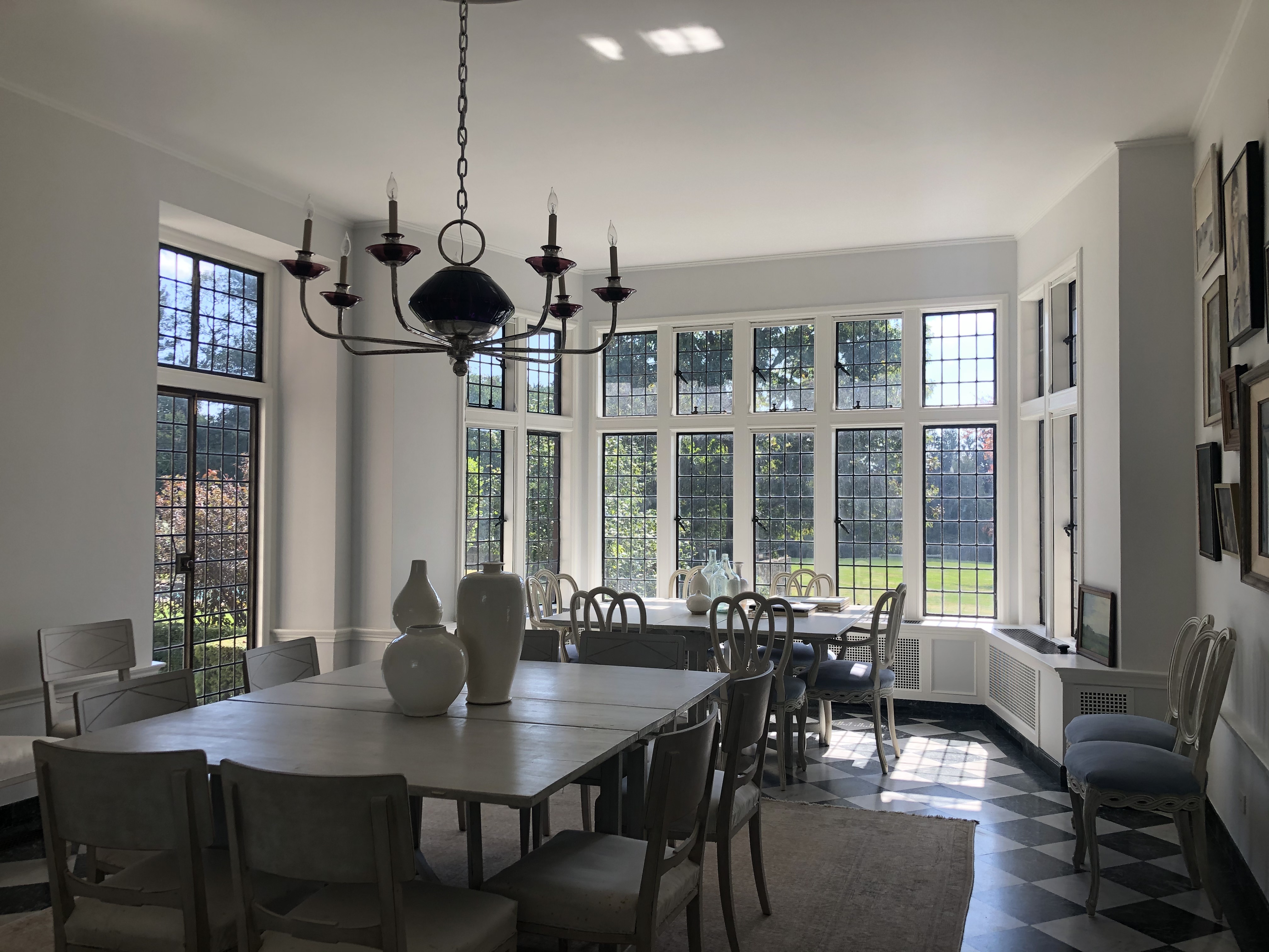 An internal view at Foundation House in Greenwich, CT, with a candle chandelier, dining table, and large windows looking out on a lawn.