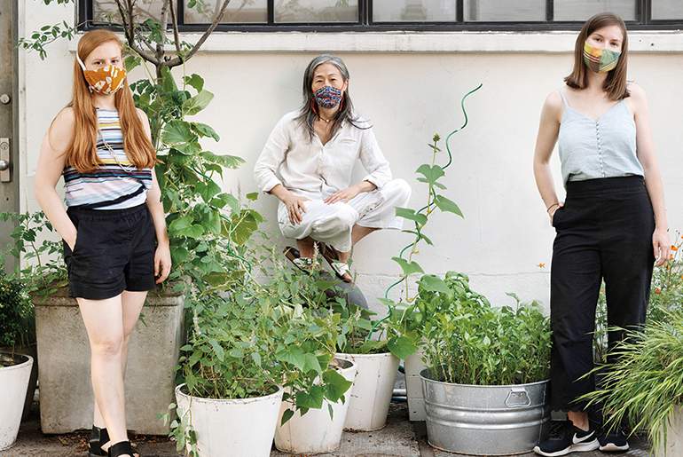 Image of three people in facemasks against a white wall with green plants in pots