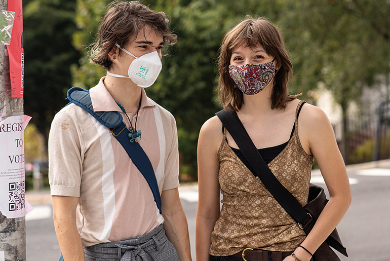 Image of two people in facemasks dressed for warm weather