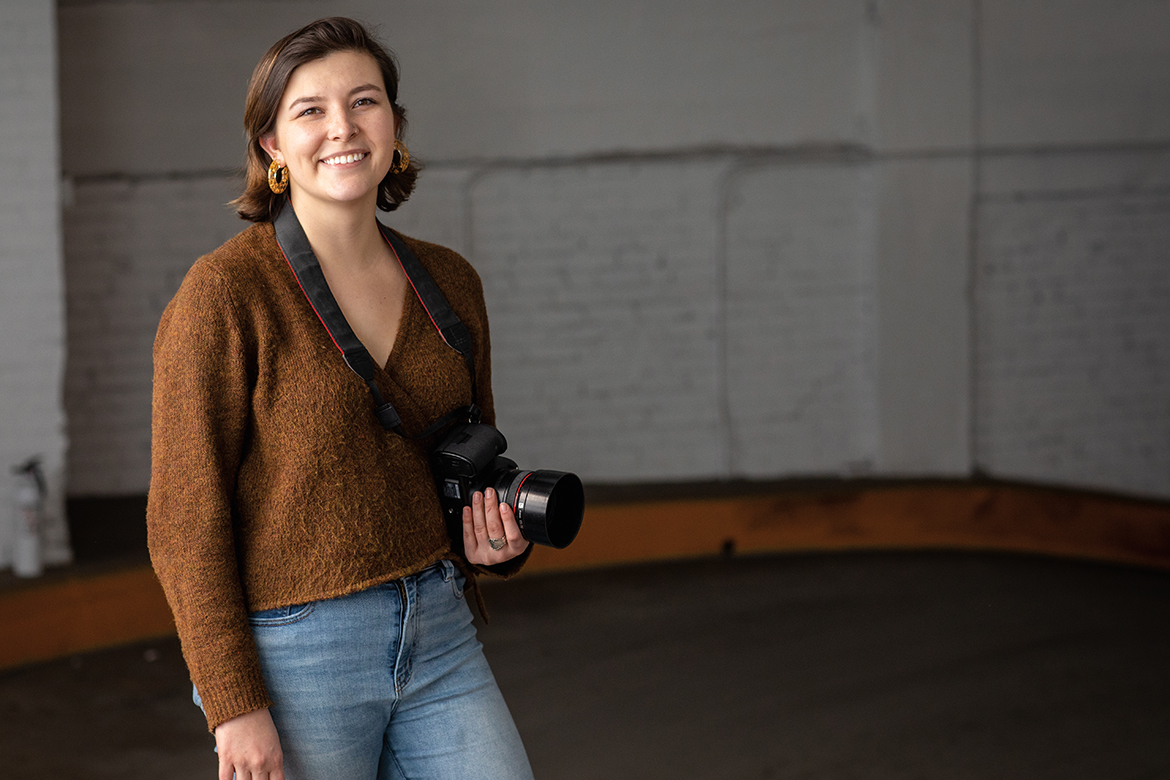 Image of a female in a brown sweater and jeans holding a camera