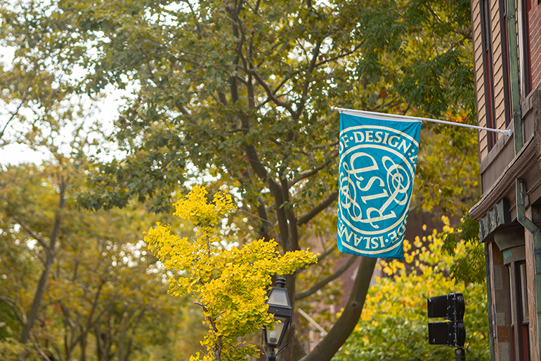Image of a building and trees with a teal RISD seal flag 