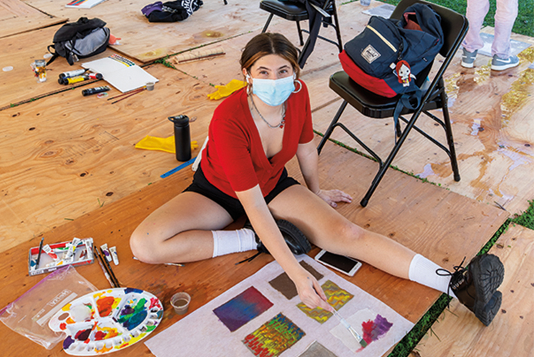 Image of a female in a red shirt and shorts working in an outdoor art studio 