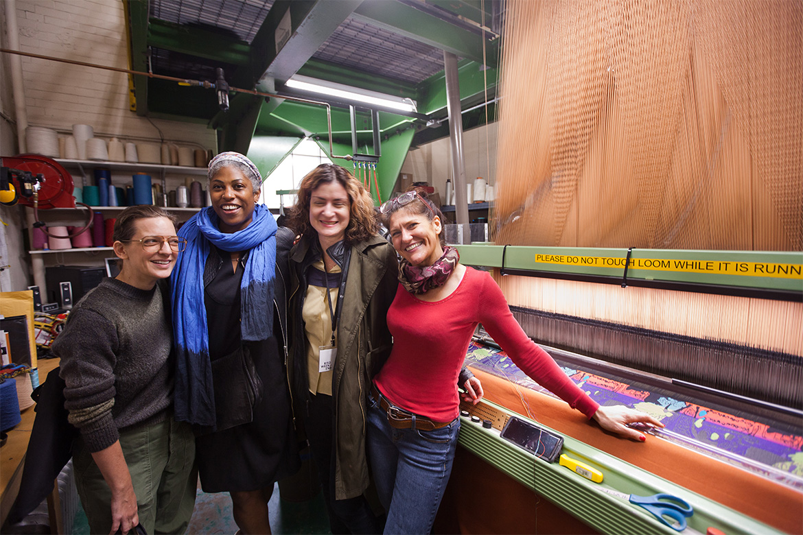 Polly Spenner 10 T X, right, standing with guests in front of the jacquard loom in the Metcalf Building at RISD Weekend 2019.