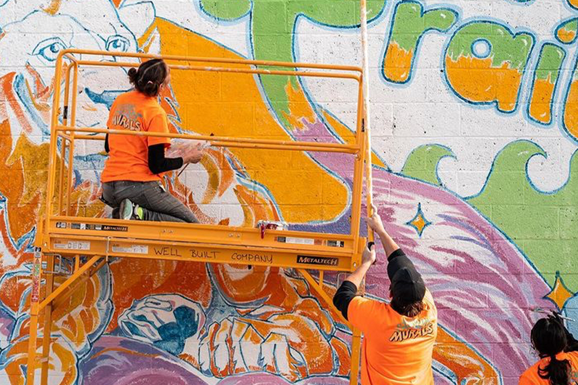 Three people working on a mural in shades of green, orange, and purple