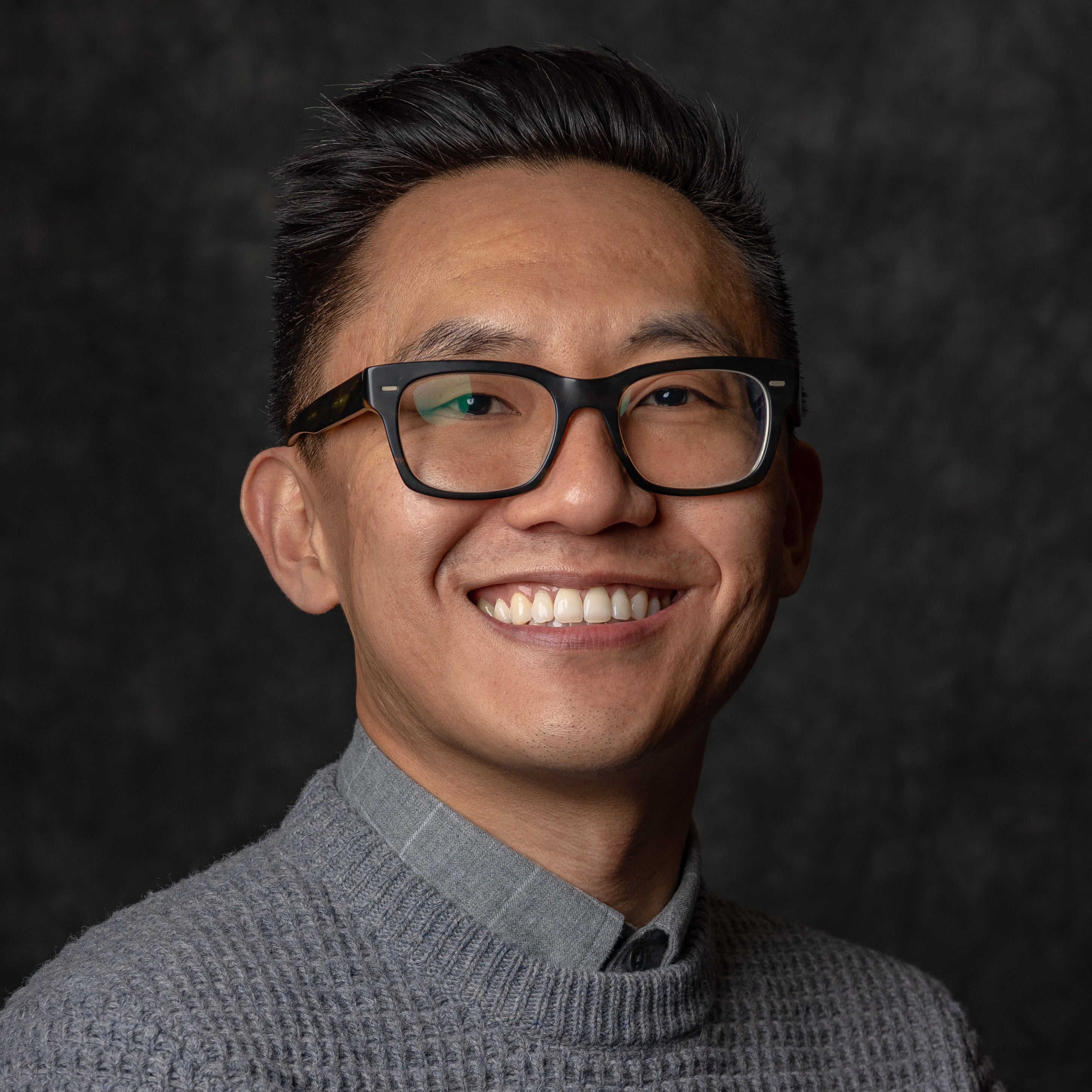 Marc Choi Image of a male in glasses with dark hair in a grey button up shirt and sweater