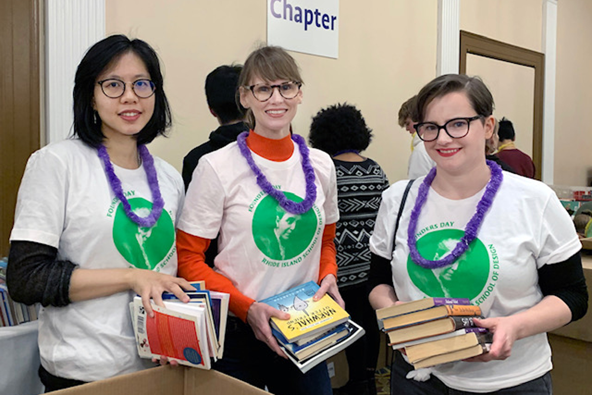 Three females with white and green shirts holding books with purple leis around their necks