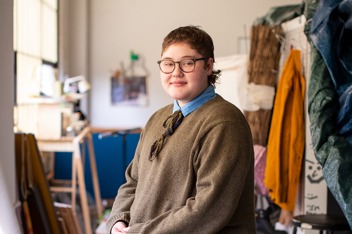 Person with short hair glasses and brown sweater in a studio