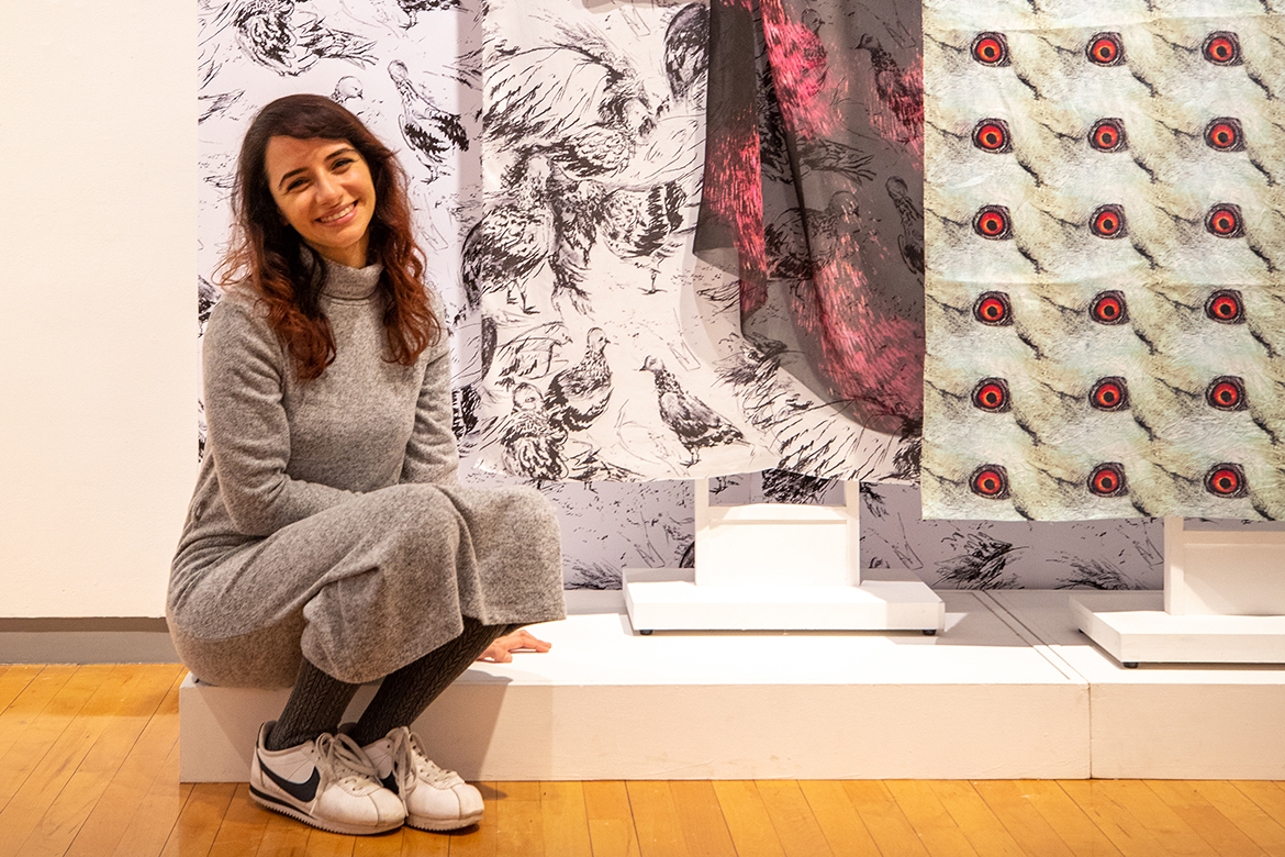 Dina Khorchid sitting in front of an exhibition of her work 
