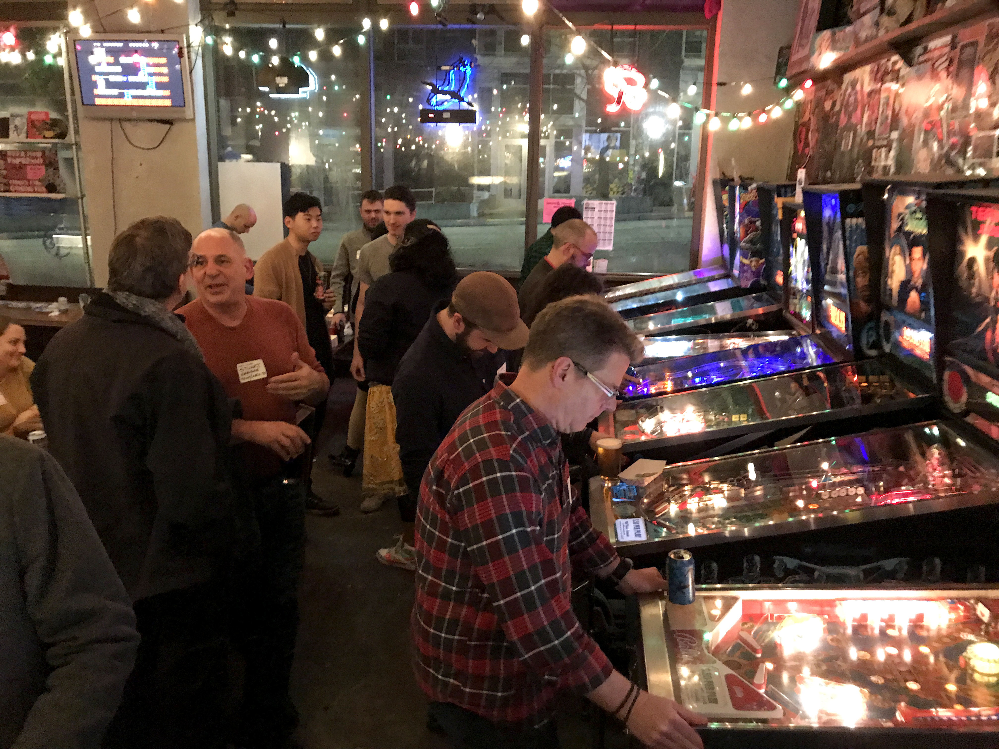 A group of people conversing while others play on pinball machines