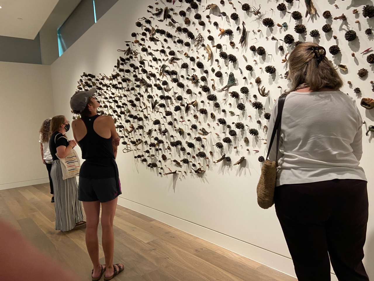 Three alumni looking at a sculpture of bronze pinecones and forest debris affixed to a wall