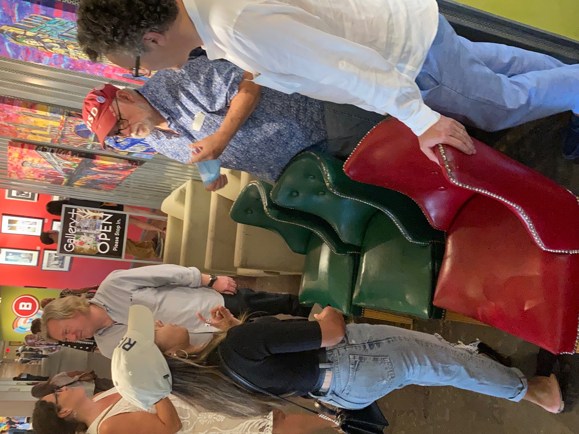 Four people speaking to each other around two green chairs and a red one