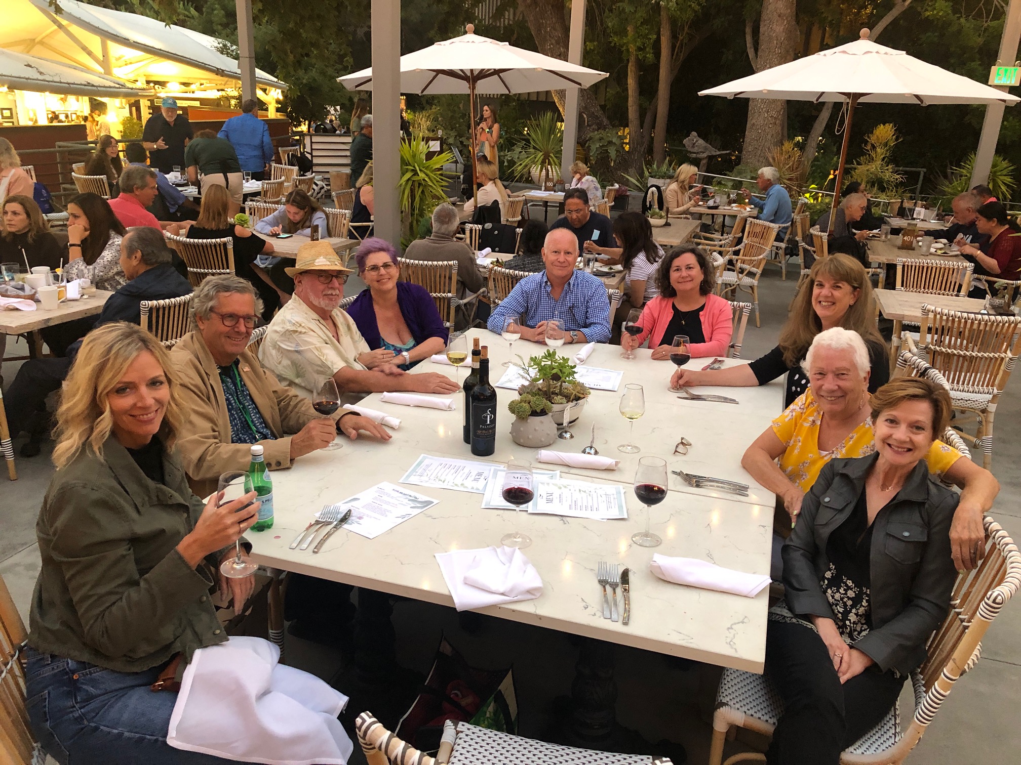 Nine people smiling and gathered around an outdoor dining table