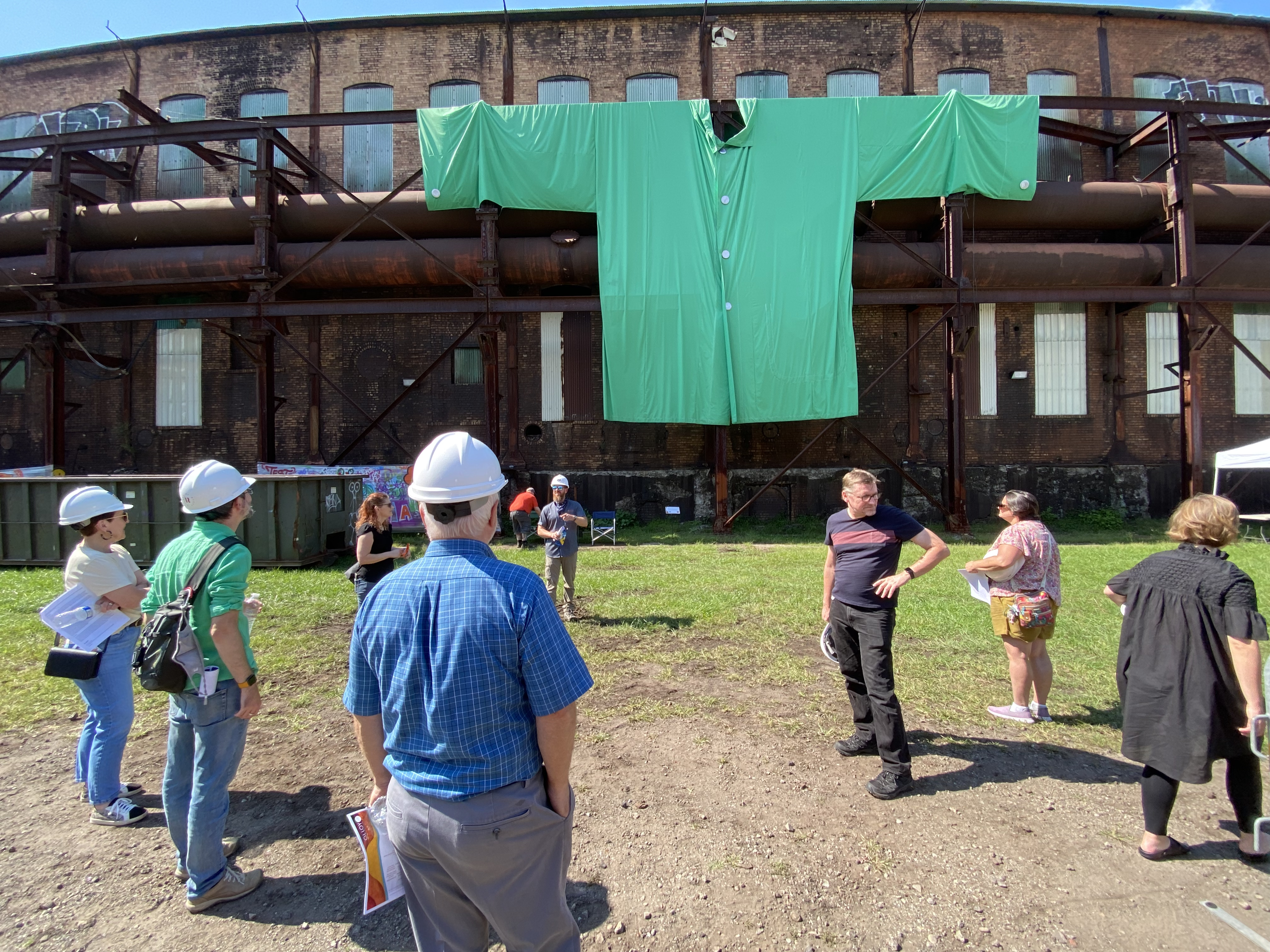 Nine people standing under a large green T-shirt hanging outside