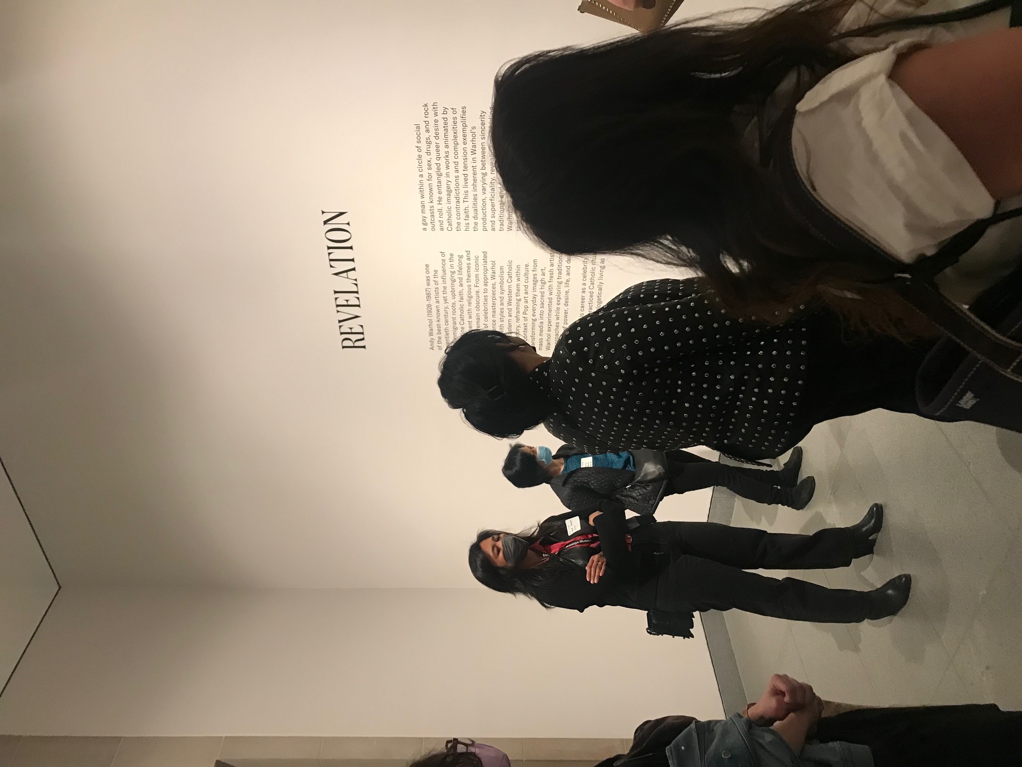 Five people looking at black text on the white wall of a gallery