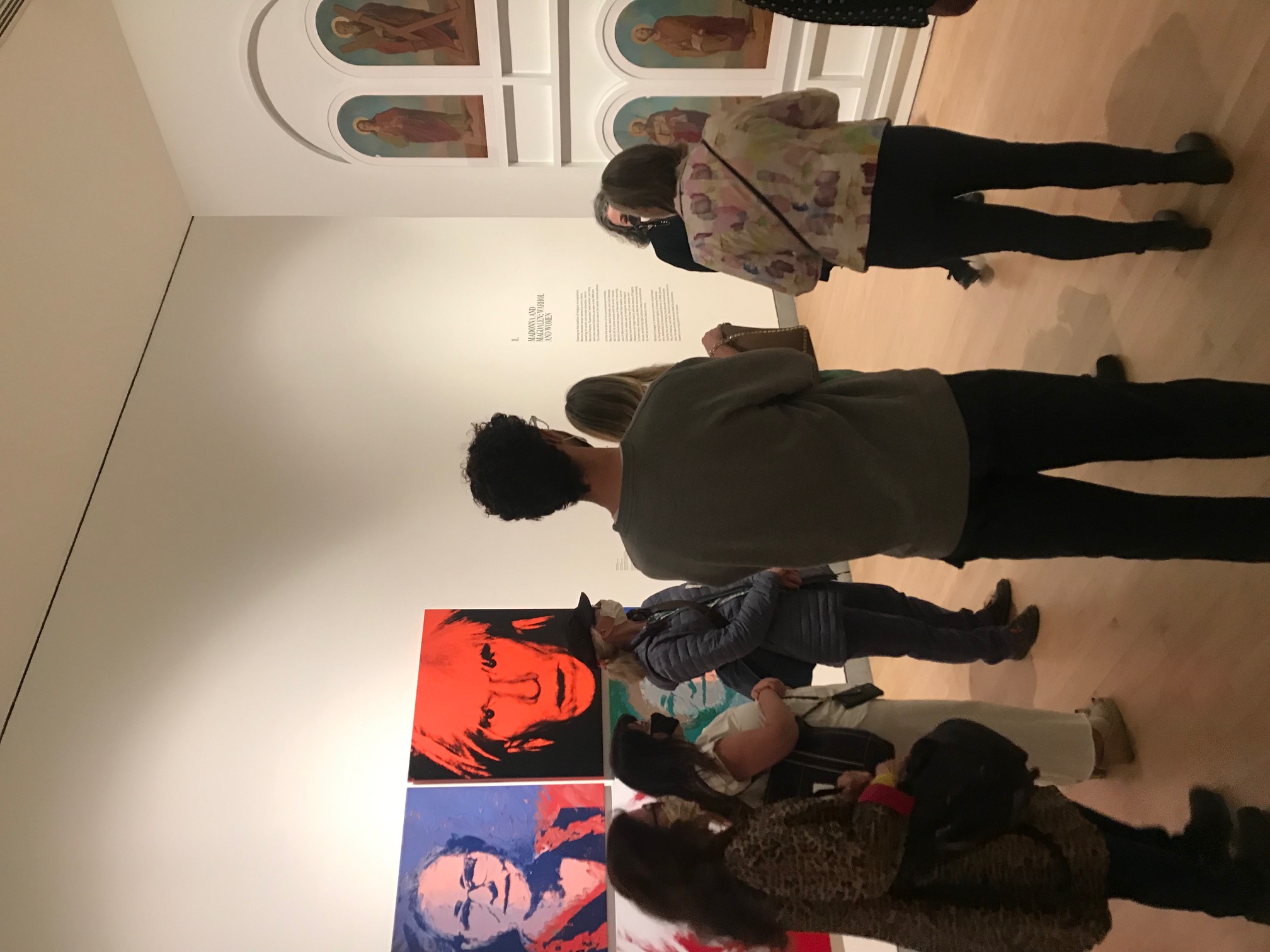 Eight people standing in a gallery besides pop art photographs and depictions of heavenly figures