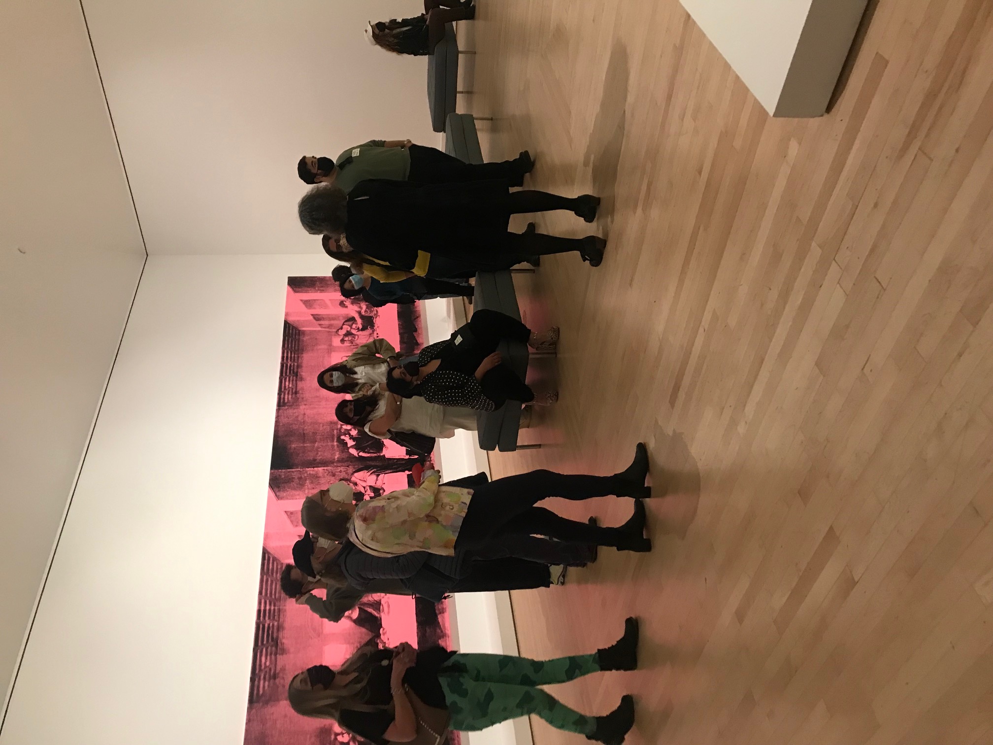 Thirteen people in a gallery and standing in front of two pink and black photograph prints on canvases