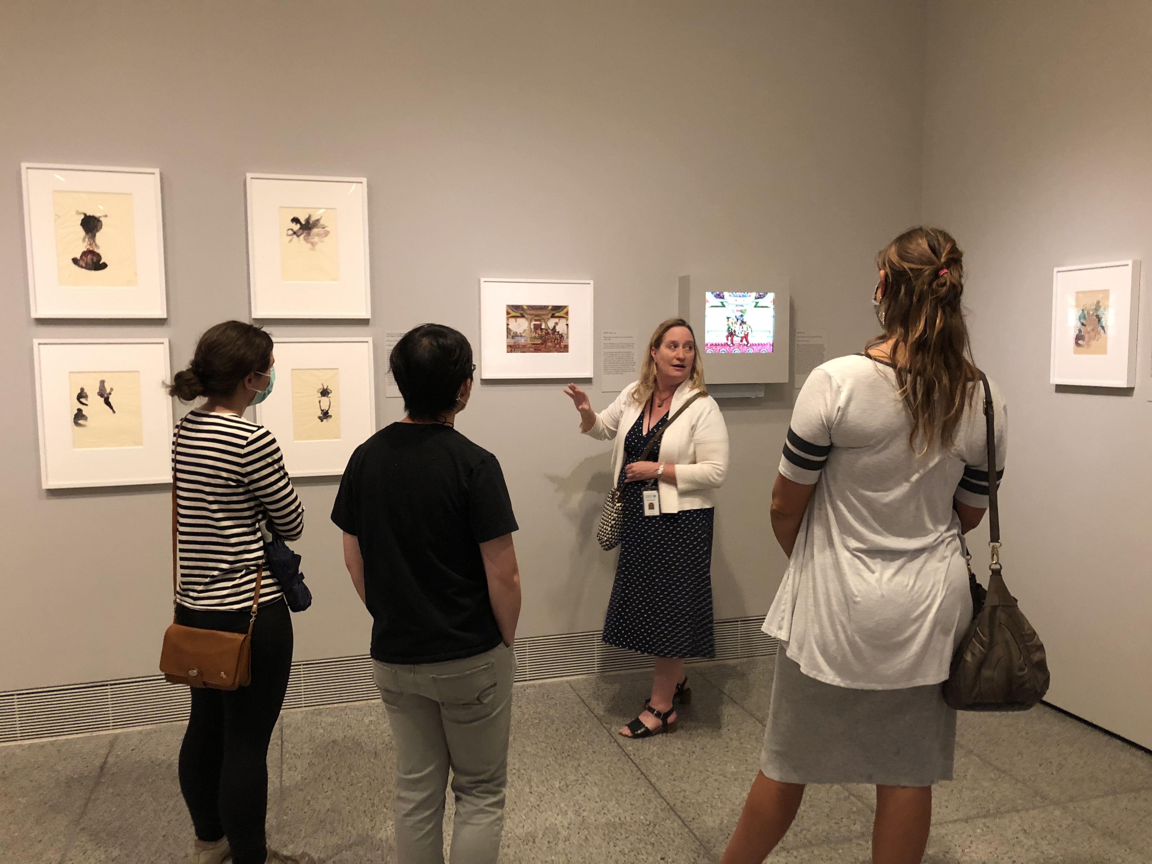 A person gesturing towards a black and tan art piece while three people observe