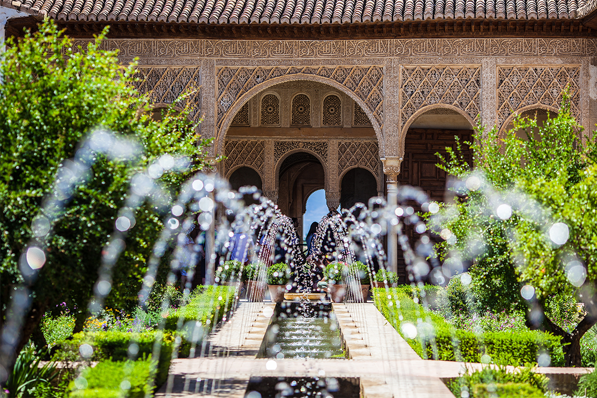 A fountain in front of a mosque and its green trees