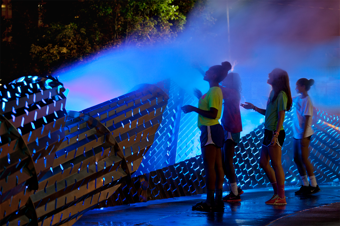 Four women examining a tall brown structure in front of an illuminated violet background