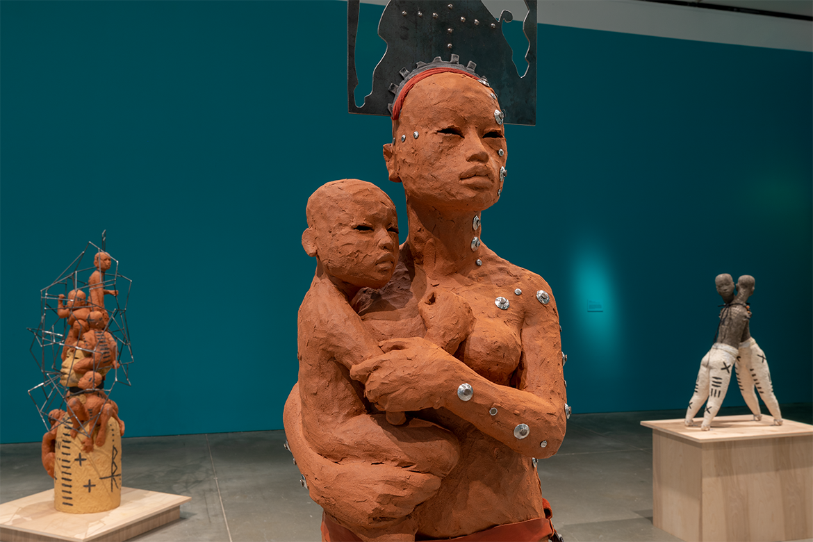 A woman sculpted from clay holding a baby sculpted from clay