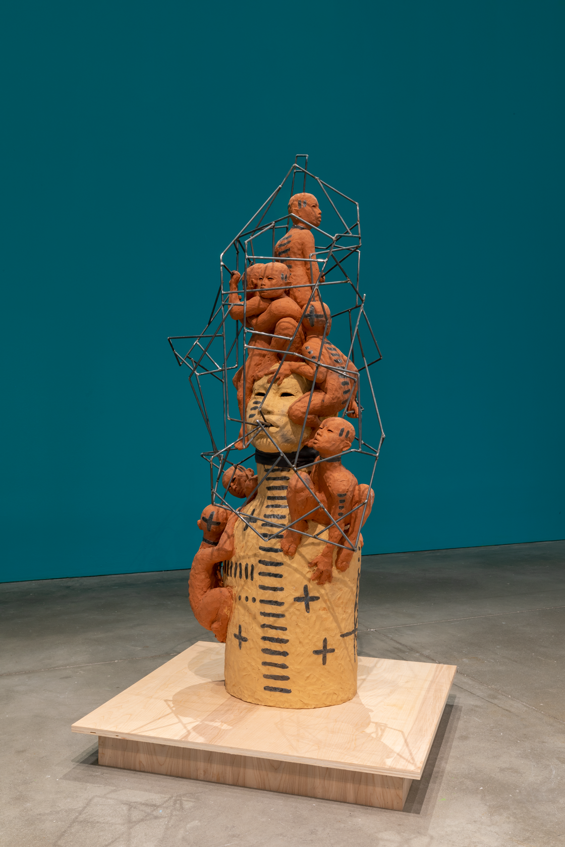 A clay bust surrounded by orange figures climbing over wire