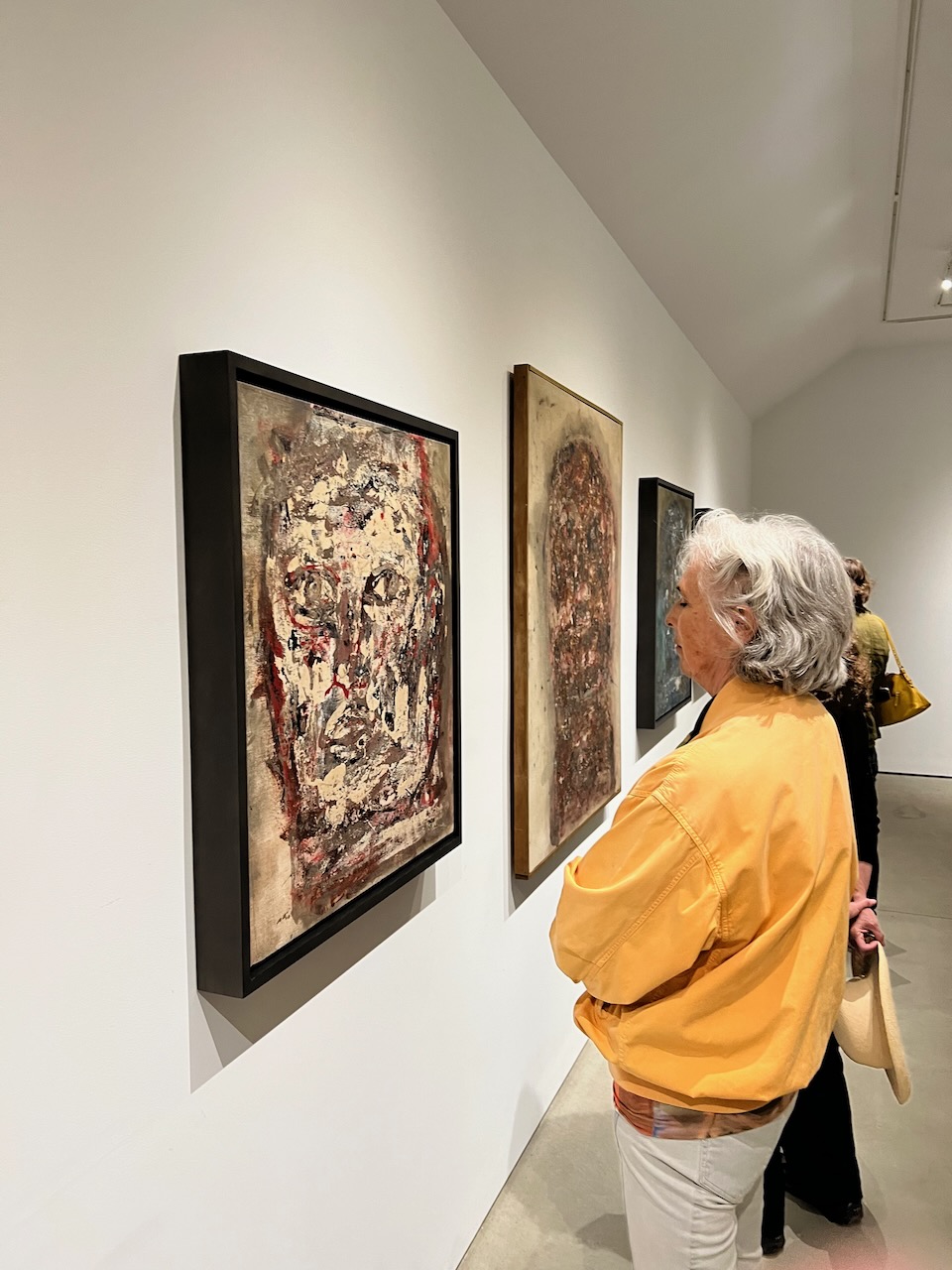 A person in a museum gazing at an abstract painting of a face
