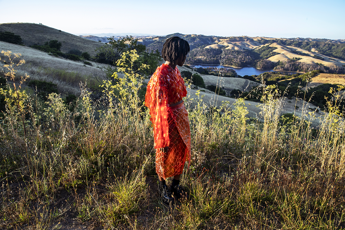 A person with short black hair and an orange robe standing in a grassy plain