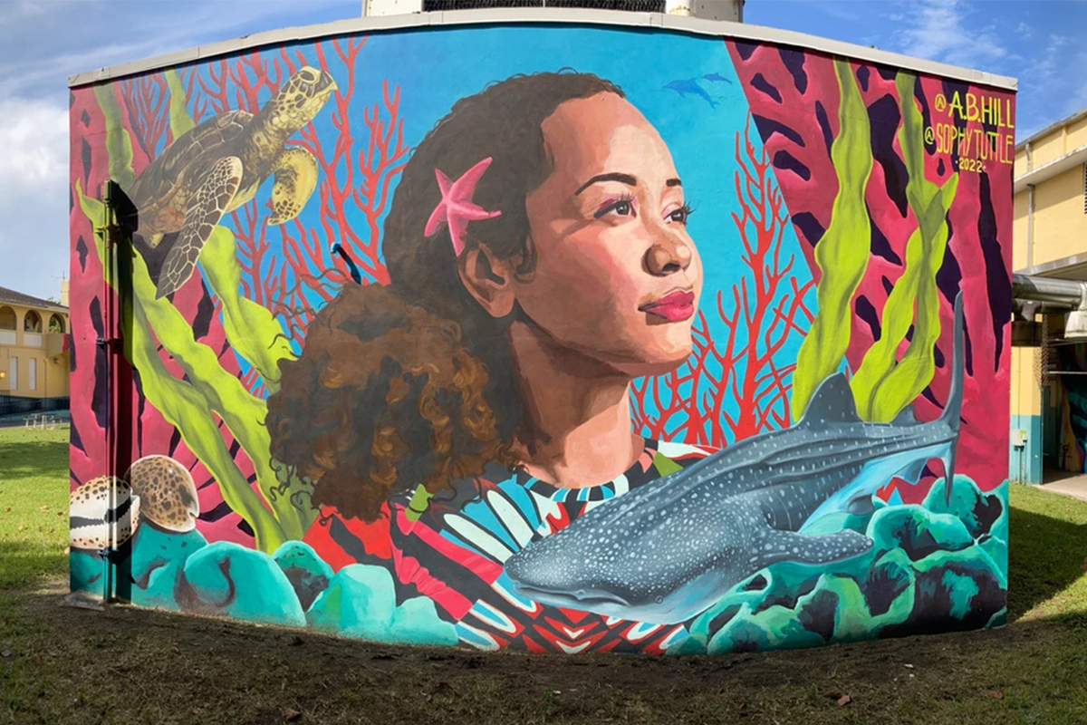 An outdoor mural of a woman surrounded by a whale and marine flora