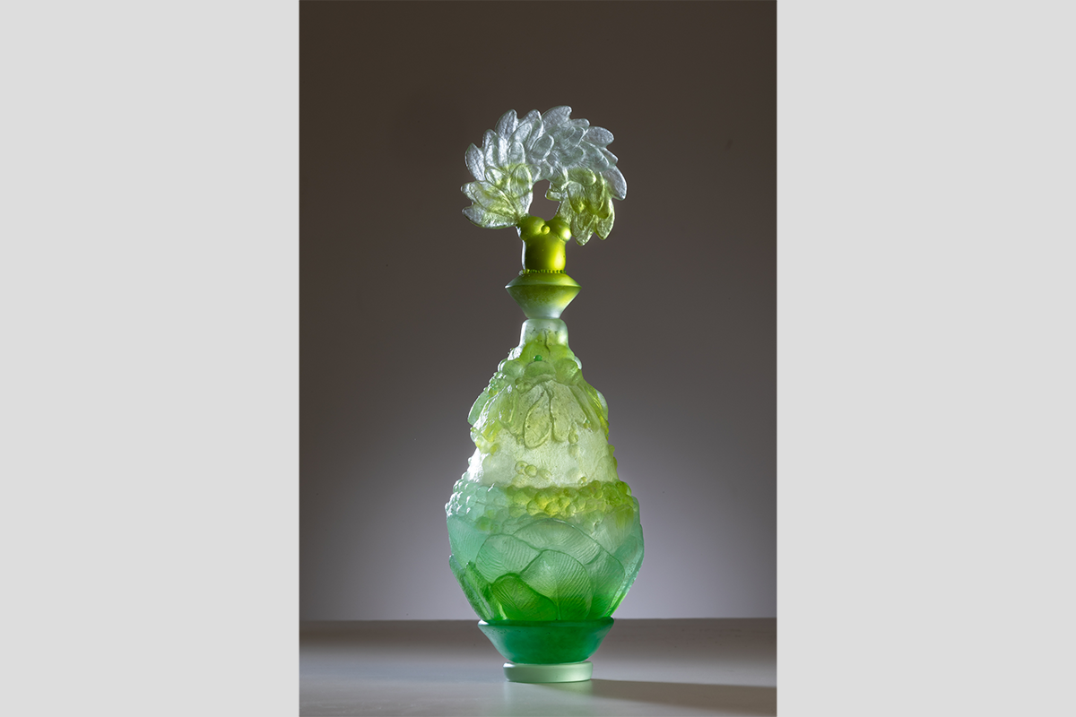 A green glass perfume bottle with a clear and green laurel at the top