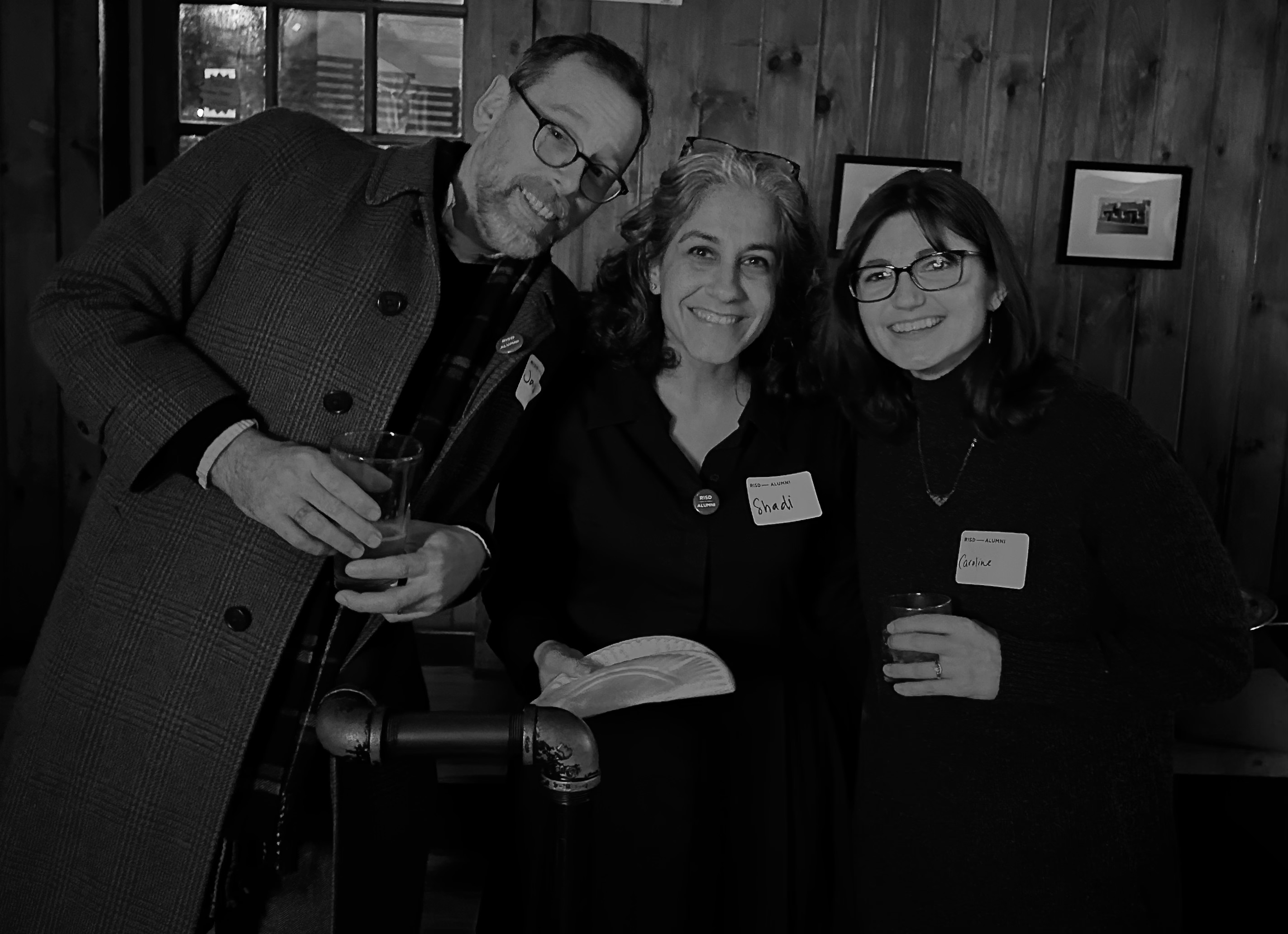 A black and white photo of people holding drinks and smiling at the camera