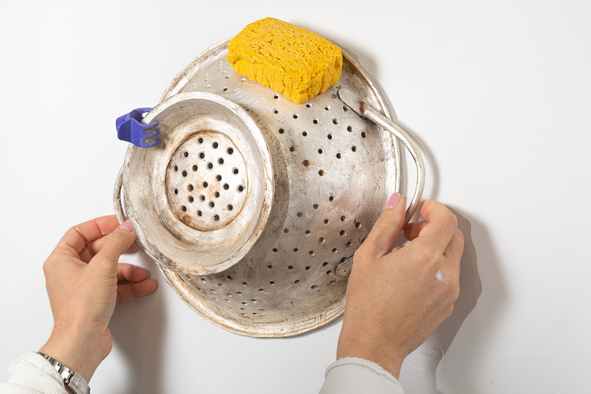 Hands holding a colander with a sponge and clip attached