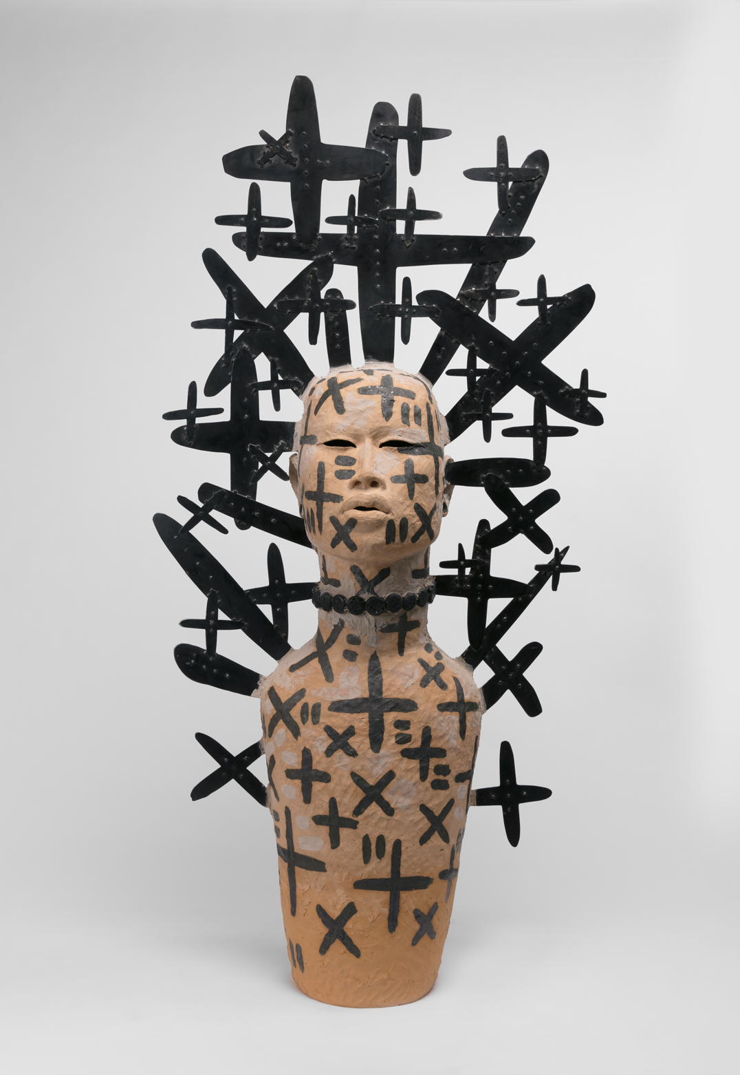 A tan bust of a person marked with black crosses and with black crosses sprouting from their body